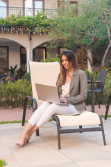 Smiling business girl working with laptop in hotel courtyard - vertical image.