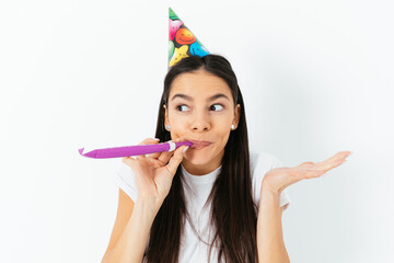 Portrait young woman in birthday cap looking aside blowing pipe