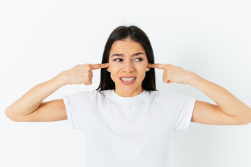 Stressed young woman wearing white t-shirt covers her ears