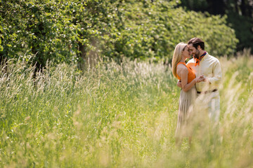 Side view of smiling couple holding hands and hugging on lawn in summer park.