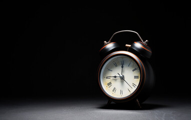 retro style black alarm clock placed on a dark table on a black background