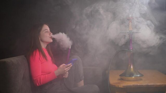 a girl in a pink jacket smokes a hookah