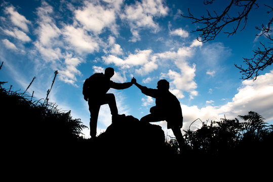 silhouette of two unrecognizable people holding hands and helping each other while doing a mountain route. Help and assistance concept.