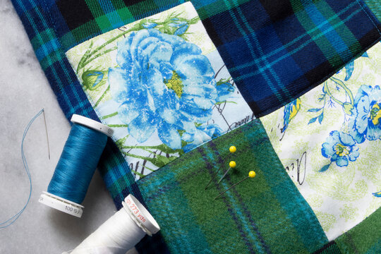 A sewing closeup of a quilted blanket with neddle and thread with blue and green squares.