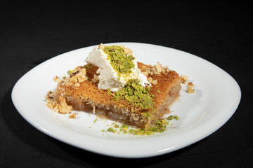 Traditional style kadayif dessert. It is served on a white plate on a black background. Top view, space for text.