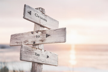 groom to be text quote on wooden crossroad signpost outdoors on beach with pink pastel sunset colors. Romantic theme.