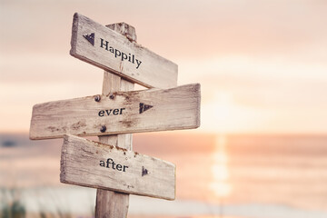 happily ever after text quote on wooden crossroad signpost outdoors on beach with pink pastel sunset colors. Romantic theme. - obrazy, fototapety, plakaty