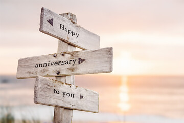 happy anniversary to you text quote on wooden crossroad signpost outdoors on beach with pink pastel...
