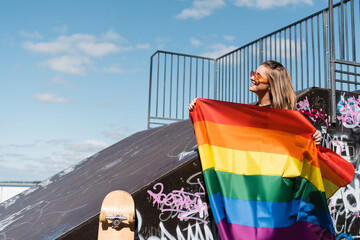 happy young woman holding lgbt flag near skate ramp and skateboard.