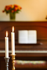 Two thin candles in candle stick holders burning against blurry piano and bouquet of flowers...