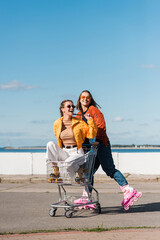 happy woman riding roller skates near friend in shopping cart.