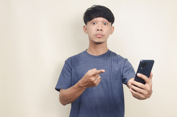 portrait of young asian shocked looking at phone on isolated background