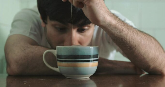 young man under the influence of drugs looks at the tea bag he dips into the cup