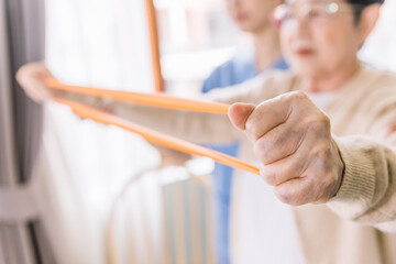 Close up hands of nurse caregiver using resistance band exercise for the senior patient in physiotherapy treatment. Home health care and nursing home concept.