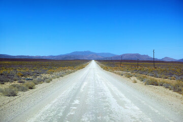 Fototapeta na wymiar Dirt road in arid and barren highland in Savanna Desert in rural South Africa with copyspace. Dry, empty, remote land against blue sky. Global warming and climate change in drought environment