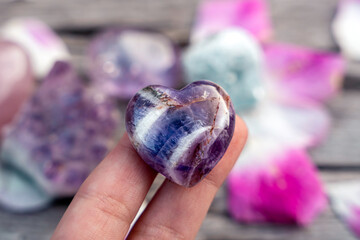 Purple amethyst crystal heart in a female hand, crystals in the background
