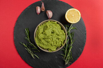 Top view of homemade organic guacamole, garlic, lemon and tortilla chips on a slate plate on a red background. Selective focus.