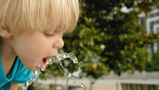 Cute little boy face portrait drink water in a park from drinking fountain slow motion