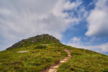 Fototapeta premium Girl tourist climbs the path to the top of the mountain. Beautiful mountain landscape with cloudy sky