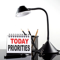 TODAY PRIORITIES text on notebook with pen and table lamp on the black background