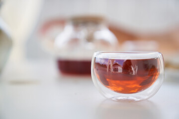 Transparent glass Cup of tea in nature. The concept of breakfast in the backyard of the house. Early morning, tea and kettle. In the cup you can see the reflection of the sky and a one-story house.