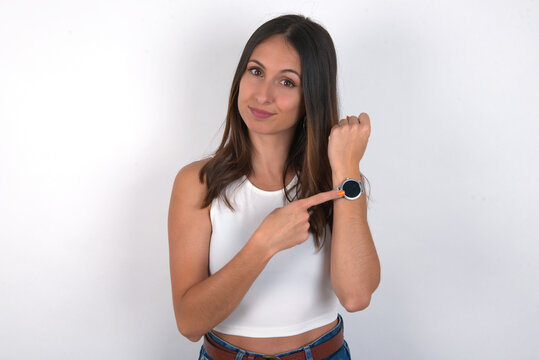 young beautiful caucasian woman wearing white top over white background in hurry pointing to watch time, impatience, upset and angry for deadline delay