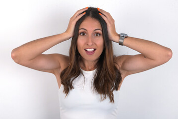 Naklejka premium Cheerful overjoyed young beautiful caucasian woman wearing white Top over white background, reacts rising hands over head after receiving great news.