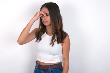 Sad young beautiful caucasian woman wearing white Top over white background, suffering from headache holding hand on her face