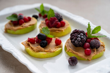 Healthy snack. Green apple rounds with peanut butter and berries