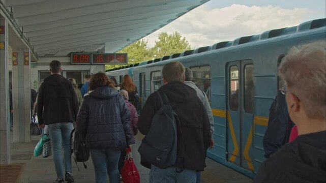 A lot of people go home from work by subway. a dense stream of people goes to the exit next to the moving subway train. clocks in the ground station of the Kyiv metro. Slow Motion 100fps 2.8k