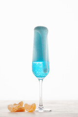 Single glass with blue champagne and tangerine on a white background. New Year or Christmas concept
