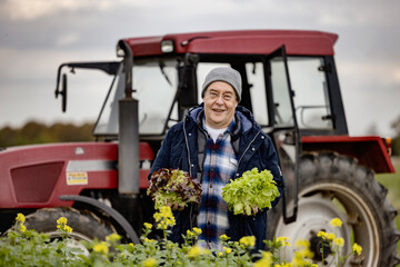 Bauer mit Salat in der Hand auf einem Feld vr seinem Traktor