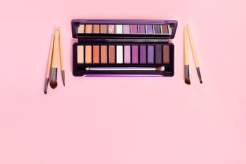Colorful eye shadow palette and set of makeup brushes on pink background with copy space. Color eyeshadow palette for day and evening eye makeup with matte and shimmer shadows