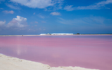 Pink lake with salt piles in the background on a blue sunny day with pink light reflection into the clouds in Yucatan town Las Coloradas