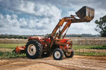 Agricultural tractor with digger and ploughing attachment at the back to till the ground in a field