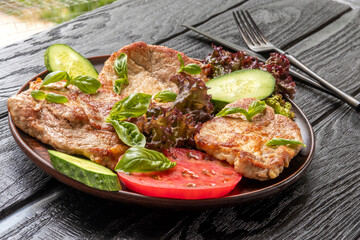 Pork chops. Supplemented with basil leaves, lettuce, tomato and cucumber slices. In ceramic plate. On black background. Hot meat dish, Homemade