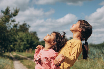 Two little girl friends raised their noses up to the sun, they enjoy the open air and freedom in the village