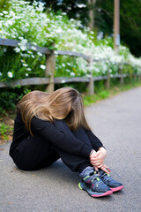 The girl hid her face in her long hair. The girl is sitting on the road near the flowers. Relaxation