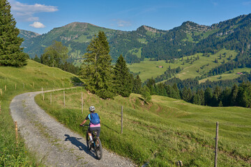 Fototapeta premium pretty senior woman riding her electric mountain bike on the mountains above Oberstaufen with Nagelfluh mountain chain in background, Allgau Alps, Bavaria Germany
