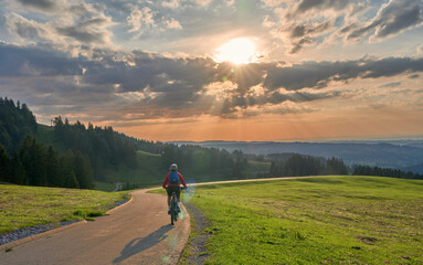 active woman riding her electric mountain bike at sunset in the Bregenz Forest mountains near...