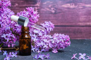 Obraz na płótnie Canvas Medicinal essential oil of lilac for aromatherapy on a brown wooden background