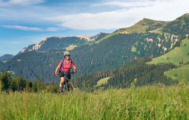 Fototapeta na wymiar pretty senior woman riding her electric mountain bike on the mountains above Oberstaufen with Nagelfluh mountain chain in background, Allgau Alps, Bavaria Germany