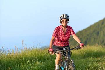 Fototapeta na wymiar pretty senior woman riding her electric mountain bike on the mountains above Oberstaufen with Nagelfluh mountain chain in background, Allgau Alps, Bavaria Germany