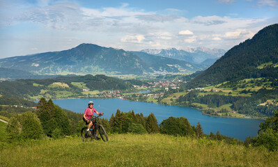 Fototapeta na wymiar beautiful senior woman riding her electric mountain bike on the mountains above Lake Alpsee near Immenstadt, Allgau,Bavaria, Germany 