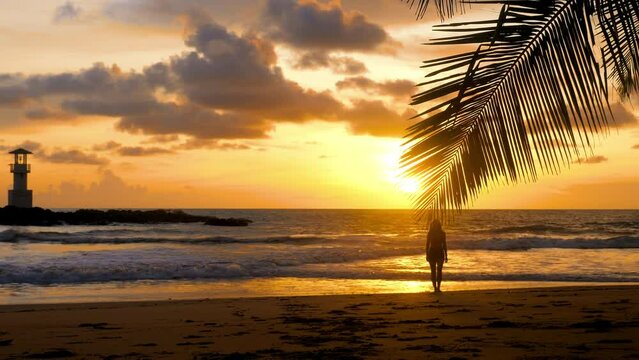 Young happy woman walking barefoot on sandy beach to palm tree branch with sea, sunset sun and lighthouse on background. Girl silhouette enjoy summer holidays. Travel, tourist, vacations concept.