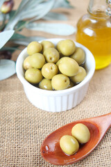 bottle of olive oil and fresh olive in a container on table .