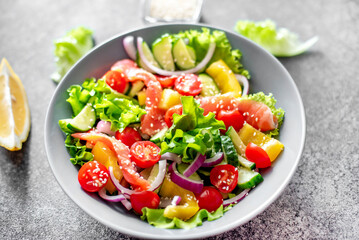 Salted salmon salad with fresh green lettuce, cucumbers, tomatoes, sweet peppers and red onions on a stone background. Ketogenic, keto or paleo diet lunch bowl.