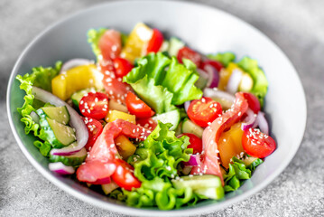 Salted salmon salad with fresh green lettuce, cucumbers, tomatoes, sweet peppers and red onions on a stone background. Ketogenic, keto or paleo diet lunch bowl.
