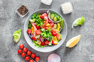 Salted salmon salad with fresh green lettuce, cucumbers, tomatoes, sweet peppers and red onions on a stone background. Ketogenic, keto or paleo diet lunch bowl.