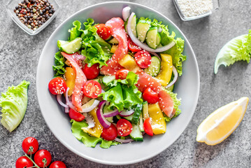 Salted salmon salad with fresh green lettuce, cucumbers, tomatoes, sweet peppers and red onions on a stone background. Ketogenic, keto or paleo diet lunch bowl.
